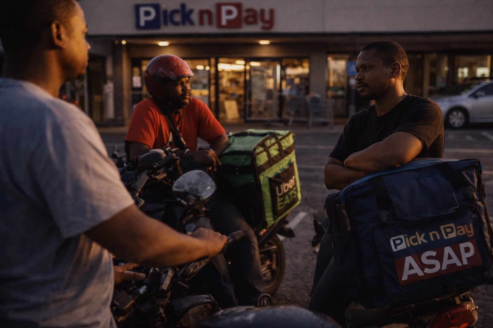 Three delivery riders in conversation outside a Pick n Pay
