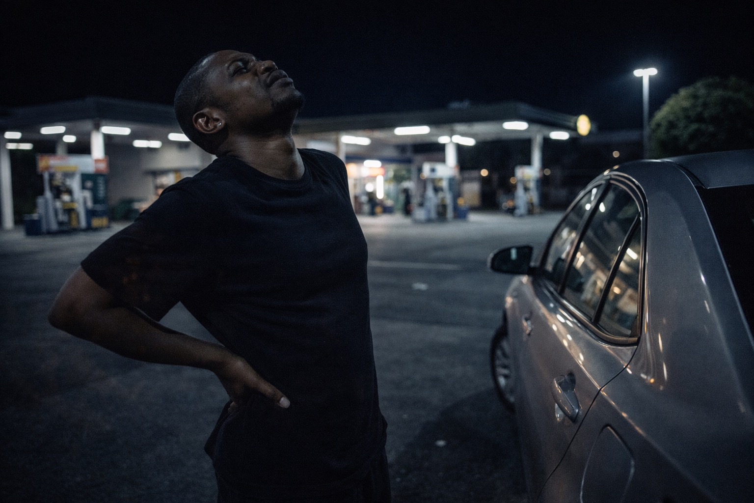 A driver stretching at a petrol station deep into the night, hours into the shift