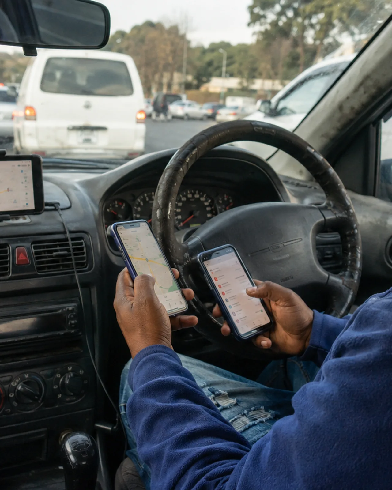 A driver at the wheel with two platform phones in hand