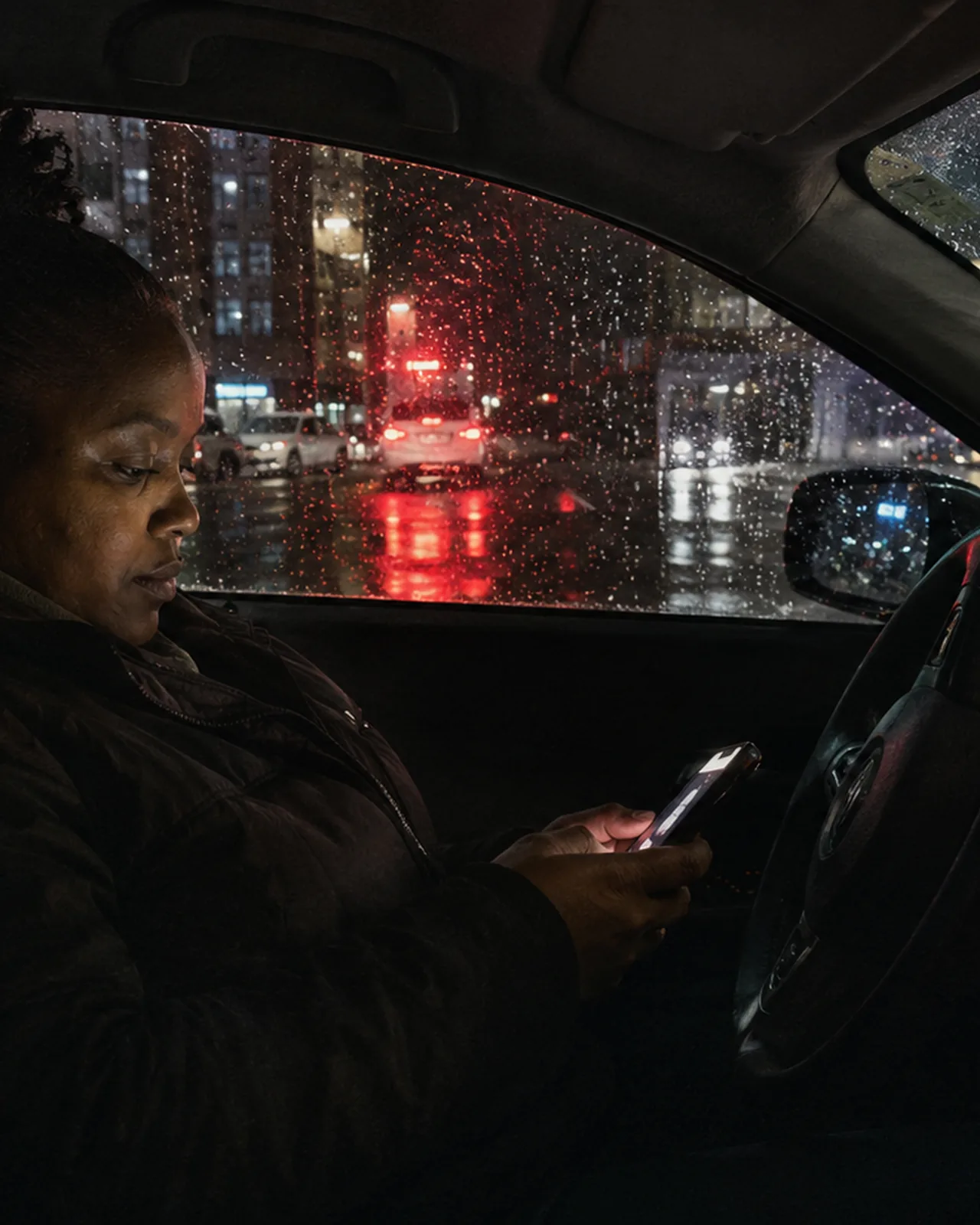 A driver at the wheel at night, phone in hand at the lights