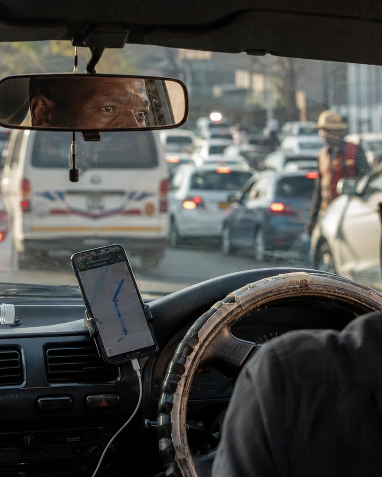 A phone mounted on the dash, the road ahead in traffic
