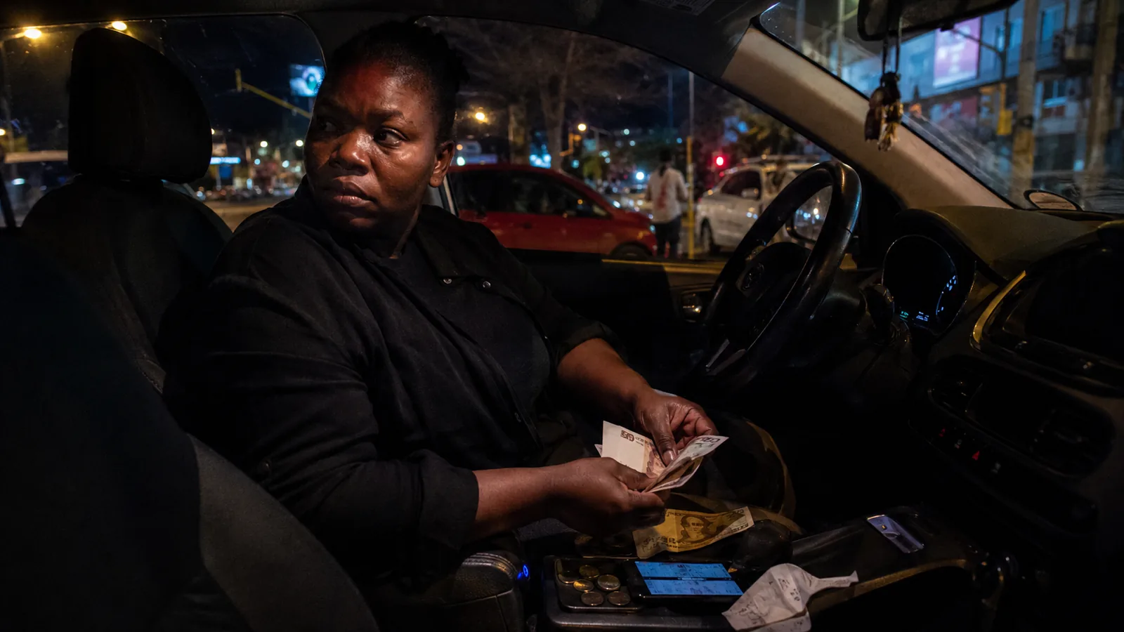 A driver counting notes at the wheel at night
