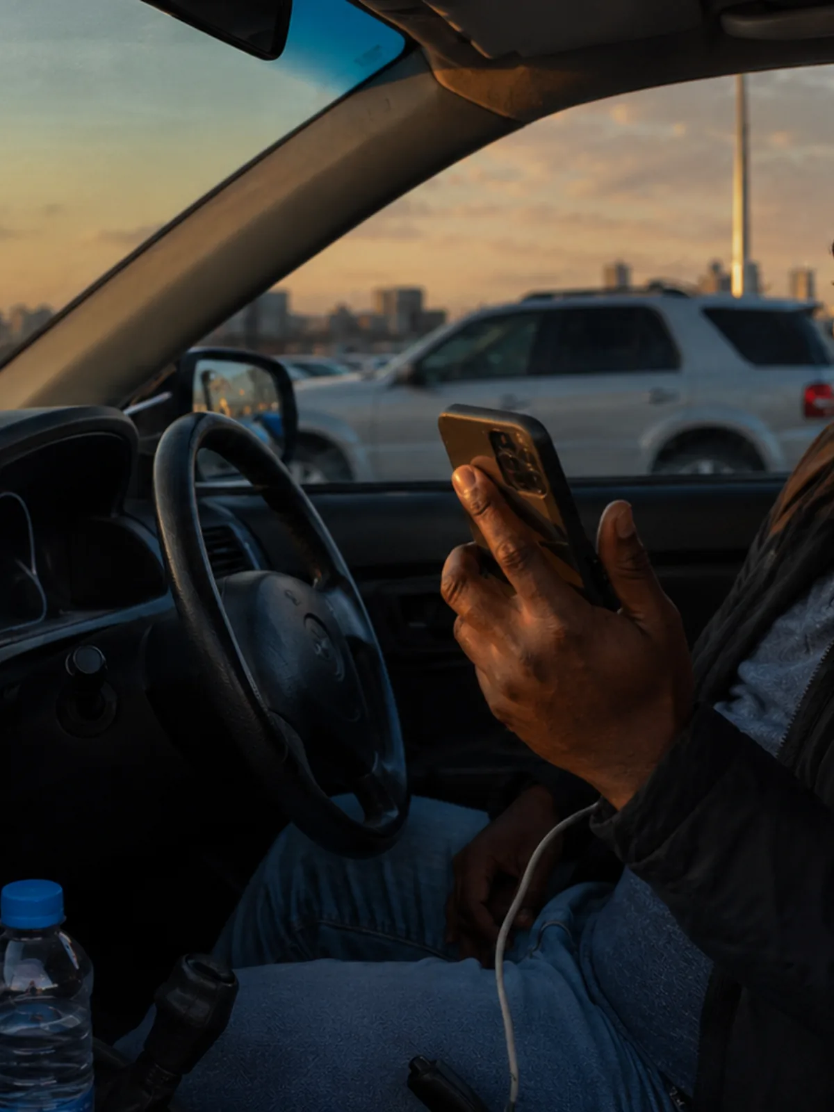 A driver checking his phone at the wheel at sunset